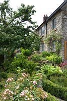 Small cottage garden with Roses in low  Buxus parterre and rasied bed of herbs next to stone house