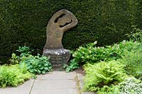 Path leading to sculptural stone seat by Taxus hedge 