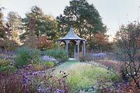 Pavilion surrounded by dramatic autumn planting of grasses, Verbena, Gaura and Asters. Radcot House, Oxfordshire, UK.