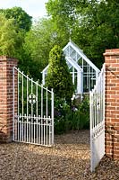 Ornate gates leading to cottage garden with white greenhouse. 