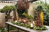 Outdoor table display made with: twisted branches of Corylus avellana 'Contorta' - Harry Lauder's Walking Stick and cut branches of Abies nordmanniana, Picea pugnes 'Hopsii', Pittosporum tobira berries, pine cones, candles and mandarins