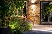 Illuminated dining area by the house surrounded by summer borders 