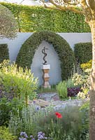 Contemporary Apothecary Garden. Sculpture of Aesclepius' staff framed by topiary Taxus baccata - Yew, in foreground mixed herb beds: Rosmarinus officinalis -  Rosemary,  Mentha piperata - Peppermint, Papaver rhoeas - Field Poppy, 