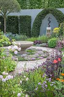 Contemporary Apothecary Garden with large water-basin. Edible herb-lawn of Thymus serpyllum varieties syn. thyme. Sculpture of Aesclepius' staff, the symbol of healing, framed by topiary Taxus baccata syn. clipped yew. Allium schoenoprasum syn. chives. Rosa syn. rose. Papaver rhoeas syn. field-poppy. Digitalis syn. foxglove. Lavandula viridis syn. green lavender, lemon lavender. Lavandula dentata 
