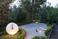 Landscape art with lighting, set on terrace with low hedging with trees beyond