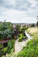 Roof garden, couple taking pictures near bridge, paved area with seating with trees and views of city beyond