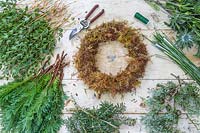 Tools, moss wreath form and prepared foliage and flowers on workbench. 