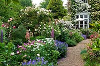 View along typically English flower border, with Rosa - Rose - arch, Geranium, Lupinus - Lupin, near gravel path to house