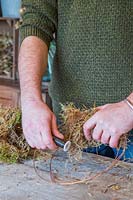 Man using floristry wire to attach moss to wire frame wreath form