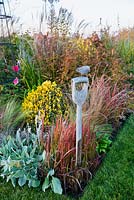 Wire bird sculpture fixed to spade handle in Autumn border, with Stachys, Imperata cylindrica and mixed Autumn plants.