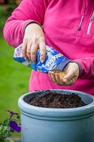 Planting up a container of bedding plants, measuring amount of compost by using a 1 litre pot to fill then calculating how much slow release fertiliser to add