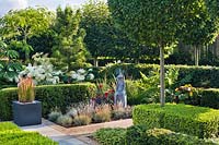 Formal planting in contemporary garden with low box and yew hedging, Imperata cylindrica 'Red Baron' in container, Carpinus betulus - Hornbeam lollipop topiary, Hydrangea arborescens 'Annabelle', Festuca glauca and statue.