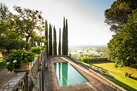 Overview of garden along terraces looking out on landscape, with swimming pool below and Cupressus sempervirens - Cypress - trees