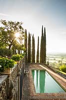 A swimming pool set in a terrace, views of Cupressus sempervirens - Cypress - trees and wider landscape 