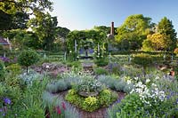 View over parterre featuring brick paths and packed colour-themed beds containing herbs and perennials