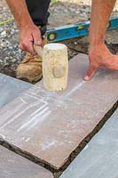 Man using rubber mallet to level paving slap on cement base