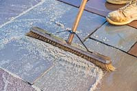 Man using brush to sweep pointing material into paving joints