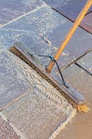 Man using brush to sweep pointing material into paving joints