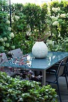 A dining corner on a terrace, plant screening from Hydrangea 'Limelight', in the foreground purple-leaved Loropetalum 'Black Pearl'