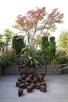 Decked roof garden with sculpture in front of planter of trees and shrubs 