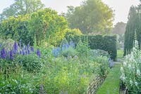 View towards house across walled garden with grass path and wide range of herbaceous perennials including Chamaenerion angustifolium 'Album', delphiniums and hollyhocks.