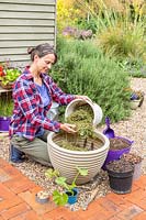Woman adding grass clippings to large plastic planter