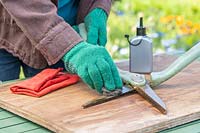 Woman wearing protective gloves whilst using wire wool to clean the blades of a pair of garden shears