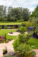 Overview of a garden with circular patio, lawn, shrub beds, summerhouse and black painted fence at boundary