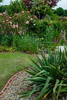Curved border edged with bricks, with gravel bed and Phormium and distant border containing Rosa 'Albertine', Cytisus battandieri - Pineapple Broom, Lupins, Nigella damascena - Love in a Mist and Papavers - Poppies - Open Gardens Day, Drinkstone, Suffolk
