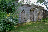 Stone ruins from a church yard in the garden, informal planting of shrubs nearby
