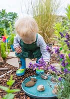 Young toddler playing with water and decorated stones in sensory garden