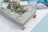 Finished pallet table with succulents on patio, with rugs and beanbag seating. 
