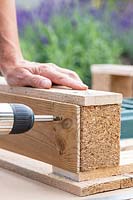 Woman using an electric screwdriver to fix planks on to the sides of the pallet to hide the planting trays. 