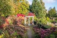 Mature garden of trees and shrubs, view along path to a classical arbor with Hydrangea in foreground