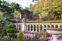 Balustrade with empty urns above a bed with Nerine, beyond a moongate and Hydrangea