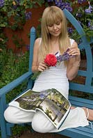 Woman enjoying aromatic scent of Lavender whilst relaxing on bench with a garden magazine - Wyken Hall, Suffolk