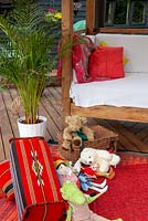 Seat and rug with cushions, kneeler and childrens' toys on garden decking with Dypsis lutescens - Areca Palm - Open Gardens Day, Bures, Suffolk