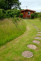 Tall grass around fruit trees left for the benefit of wildlife and insects, with path of stepping stones leading to distant summerhouse - Open Gardens Day, Kelsale, Suffolk
