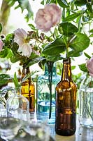 Glass bottles with foliage and flowers as table decorations