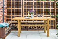 Wooden dining table and bench with built in storage for firewood, backed by fence with trellis