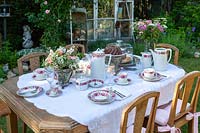 Romantic garden with laid table and wooden chairs