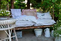 Old bed frame as a bench, pillows and a wicker table in the foreground