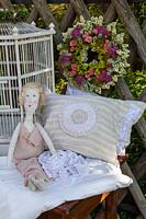 Floral wreath, bird cage, pillows and a rag doll on wooden table against a wooden lattice fence