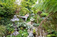 Small oriental and tropical garden with hammock, ornaments and mixed planting
