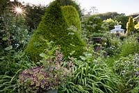 Topiary among lush planting and containers, in garden with structures including a tea house on stilts