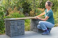 Woman placing seat made of two scaffolding boards on top of granite filled gabions.