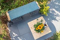 Overview of gabion and scaffolding board bench and table on slate patio in modern garden. 