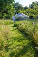 Wild flower meadow with mown path leading to yurt. 