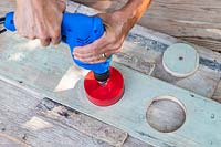 Woman using a holesaw bit to make 10cm holes in board. 
