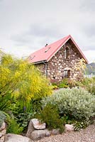 Contemporary stone and wood house with corrugated tin roof, surrounded by bold planting including Cortaderia richardii, cistus and willow at a private garden on Little Loch Broom, Wester Ross, Scotland.  